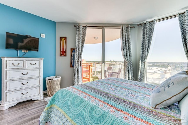 bedroom with access to exterior, expansive windows, and hardwood / wood-style floors