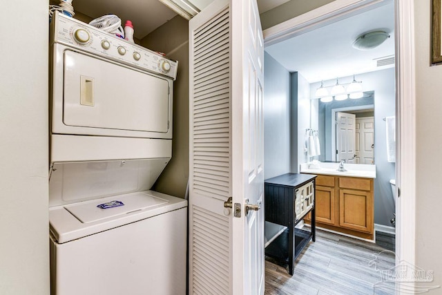 clothes washing area with sink, light hardwood / wood-style flooring, and stacked washer and dryer