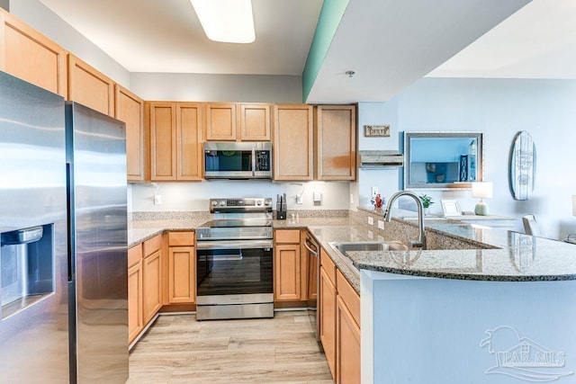 kitchen with stainless steel appliances, sink, kitchen peninsula, light wood-type flooring, and light stone counters