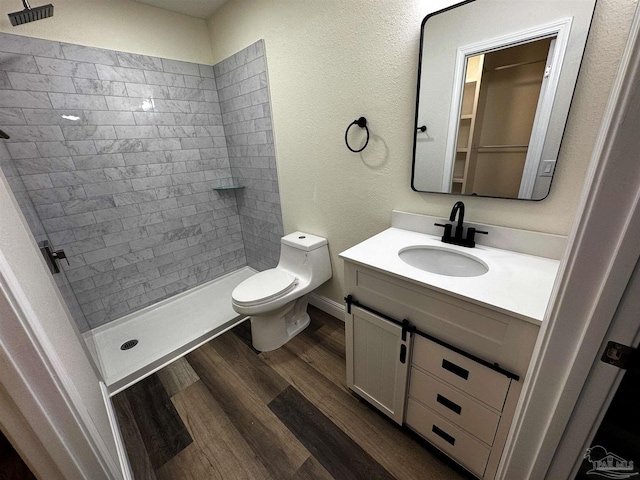 bathroom with vanity, toilet, wood finished floors, and a tile shower