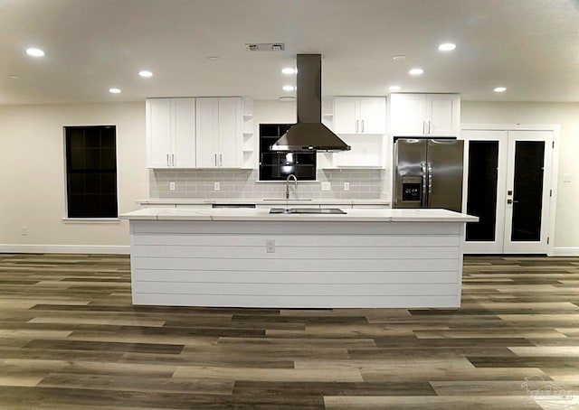 kitchen with visible vents, a center island with sink, island exhaust hood, stainless steel refrigerator with ice dispenser, and white cabinets