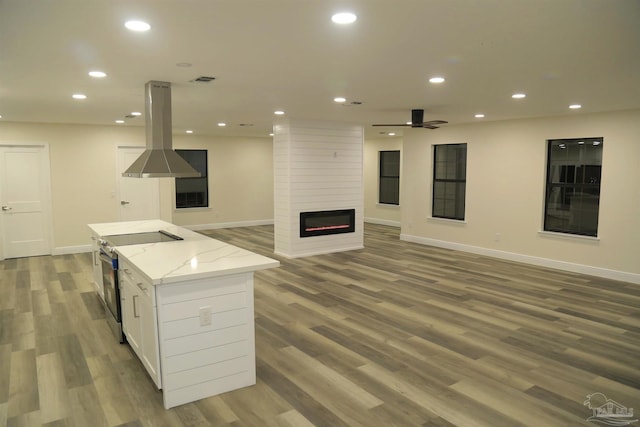 kitchen with recessed lighting, a fireplace, stainless steel range with electric cooktop, white cabinetry, and island range hood