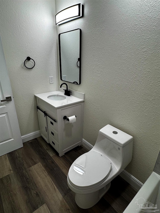 bathroom featuring toilet, vanity, a textured wall, and wood finished floors