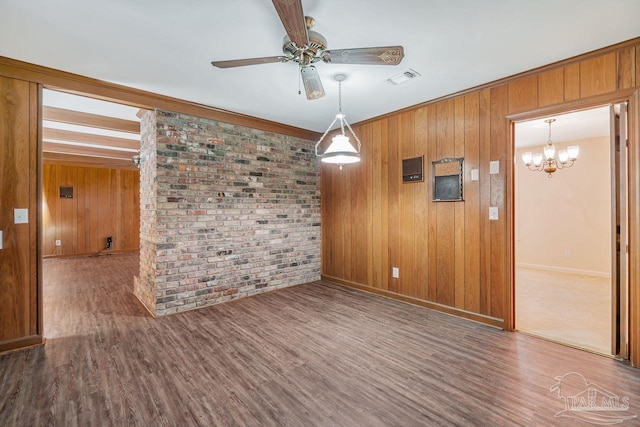 unfurnished room with ceiling fan with notable chandelier, wood finished floors, visible vents, and brick wall