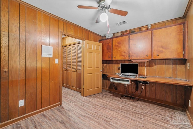 unfurnished office with a ceiling fan, visible vents, built in study area, wood walls, and light wood-type flooring