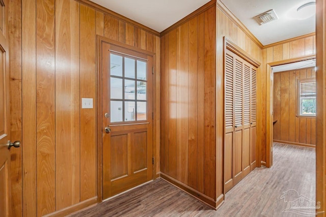 doorway with wood finished floors, visible vents, wood walls, and baseboards