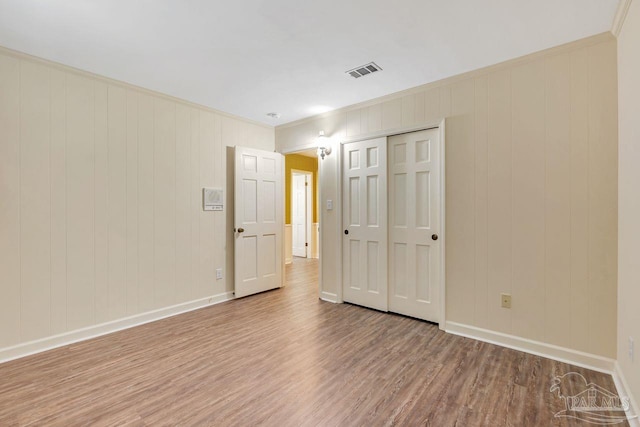 unfurnished bedroom with crown molding, wood finished floors, visible vents, and baseboards