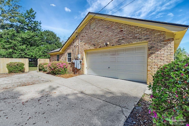 view of side of property with a garage, brick siding, driveway, and fence