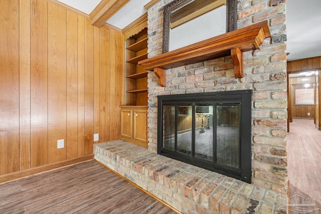 interior details featuring crown molding, a large fireplace, built in features, wood walls, and wood finished floors