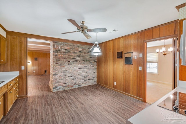 unfurnished dining area featuring ceiling fan with notable chandelier, wood finished floors, visible vents, and brick wall