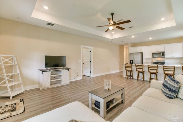 living area with a tray ceiling, light wood-style floors, a ceiling fan, recessed lighting, and baseboards