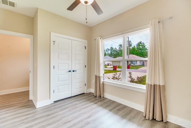 unfurnished bedroom featuring light wood-style floors, a closet, baseboards, and ceiling fan