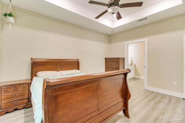 bedroom with light wood-type flooring, baseboards, ceiling fan, and a tray ceiling