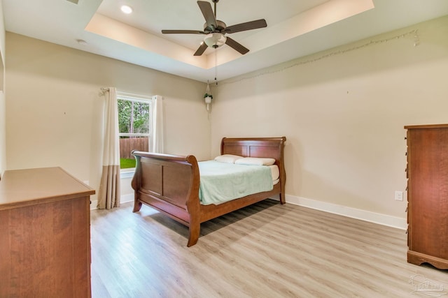 bedroom with light wood finished floors, baseboards, a raised ceiling, a ceiling fan, and recessed lighting
