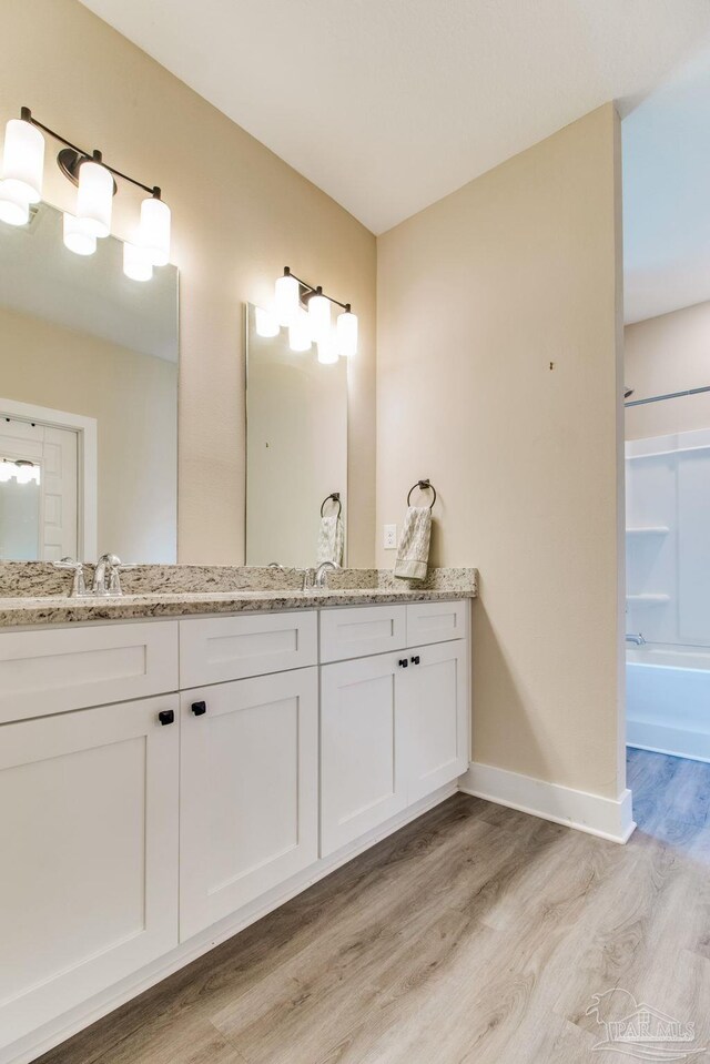 bathroom with wood finished floors, double vanity, shower / washtub combination, and baseboards