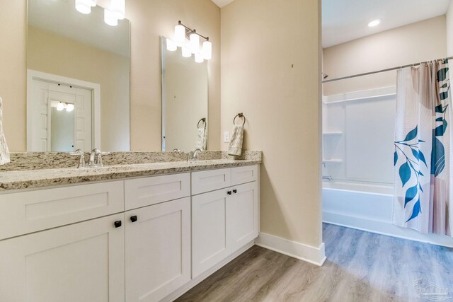 full bathroom featuring wood finished floors, shower / tub combo with curtain, baseboards, and double vanity