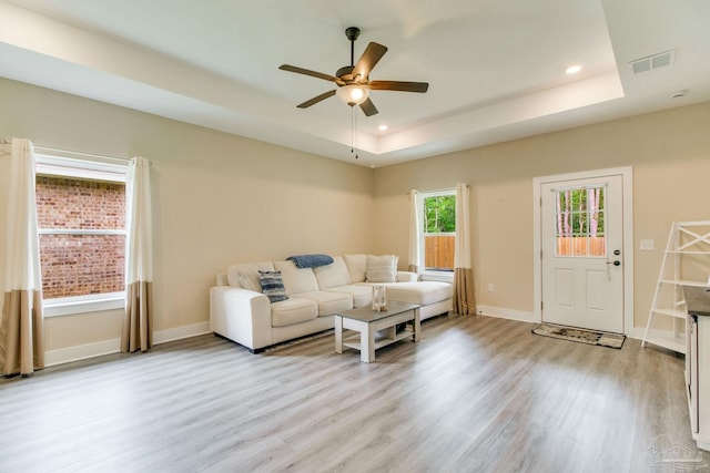 living room with light wood finished floors, a raised ceiling, ceiling fan, recessed lighting, and baseboards