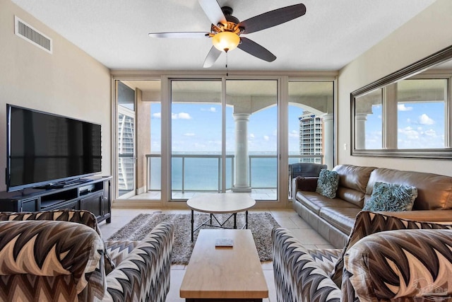 tiled living room featuring a water view, ceiling fan, and a textured ceiling