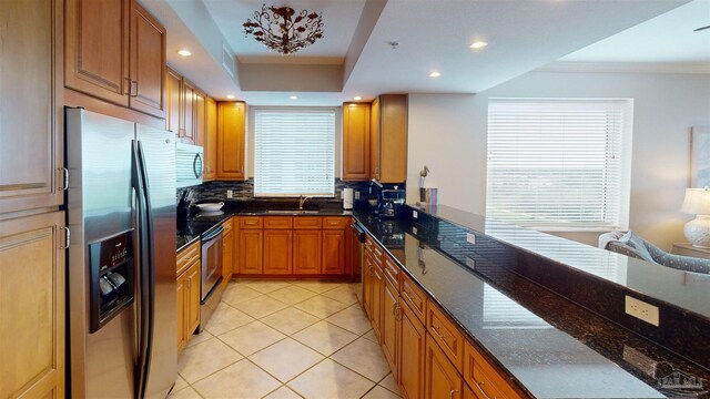 kitchen with sink, light tile patterned floors, backsplash, stainless steel appliances, and dark stone countertops