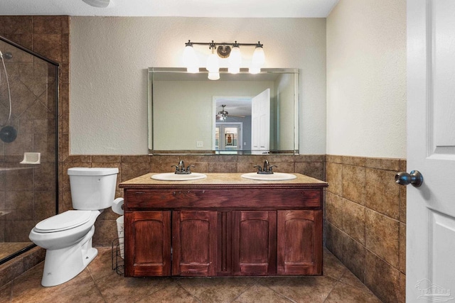 bathroom featuring tile walls, a shower with shower door, ceiling fan, vanity, and toilet