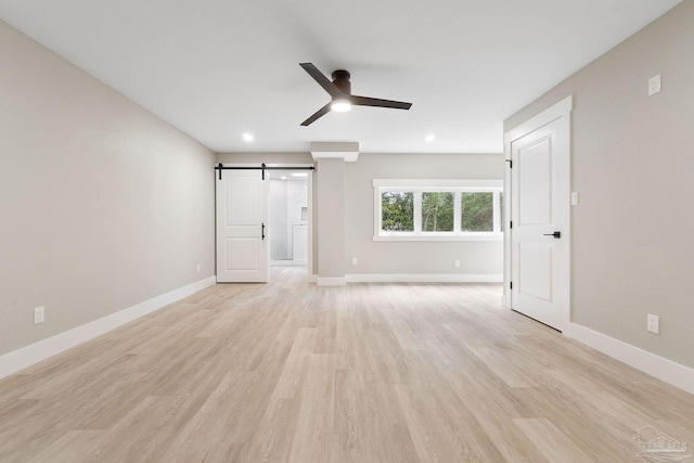 interior space with ceiling fan, a barn door, and light hardwood / wood-style flooring