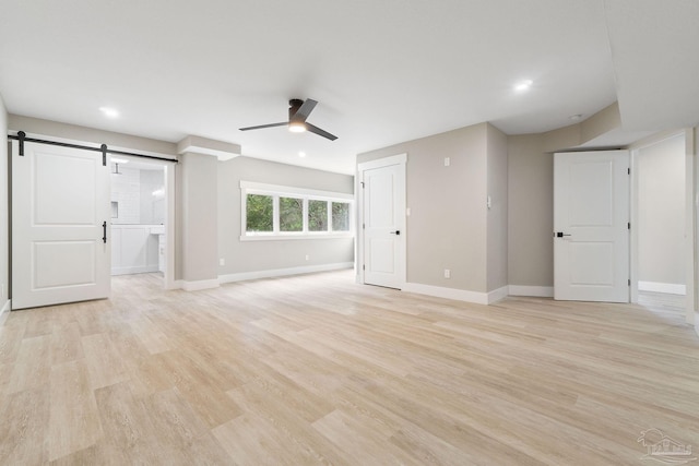 unfurnished living room featuring light wood-type flooring, a barn door, and ceiling fan