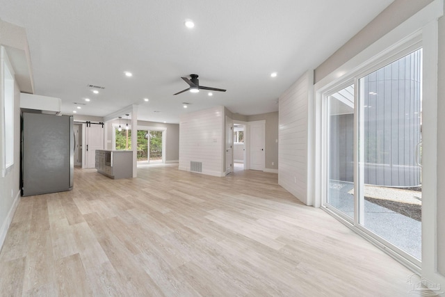 unfurnished living room featuring a barn door, ceiling fan, and light hardwood / wood-style flooring