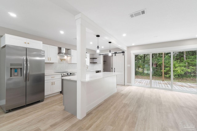 kitchen with white cabinetry, hanging light fixtures, stainless steel appliances, wall chimney range hood, and light wood-type flooring