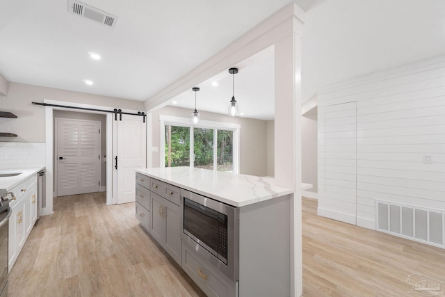 kitchen with stainless steel microwave, hanging light fixtures, a barn door, light stone countertops, and light wood-type flooring