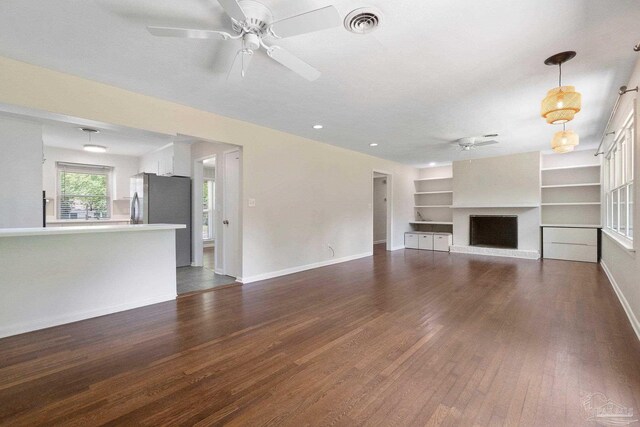 770 Connell Dr, Pensacola, FL 32503 - unfurnished living room featuring a ceiling fan, dark wood finished floors, a fireplace with raised hearth, baseboards, and built in shelves
