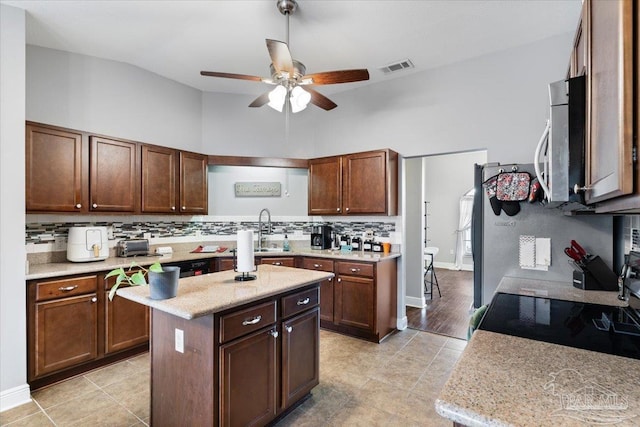 kitchen featuring sink, ceiling fan, backsplash, a center island, and light stone countertops