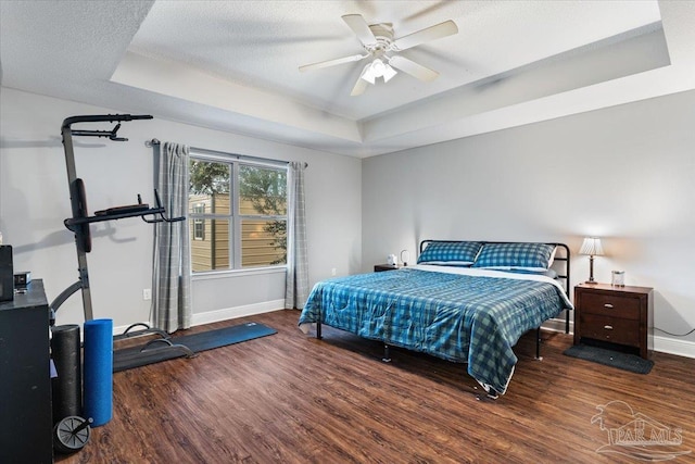 bedroom with dark hardwood / wood-style floors, ceiling fan, a tray ceiling, and a textured ceiling