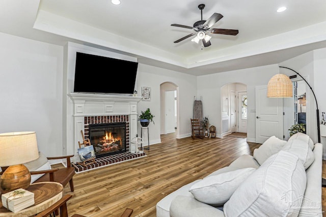living room with arched walkways, wood finished floors, a tray ceiling, and recessed lighting