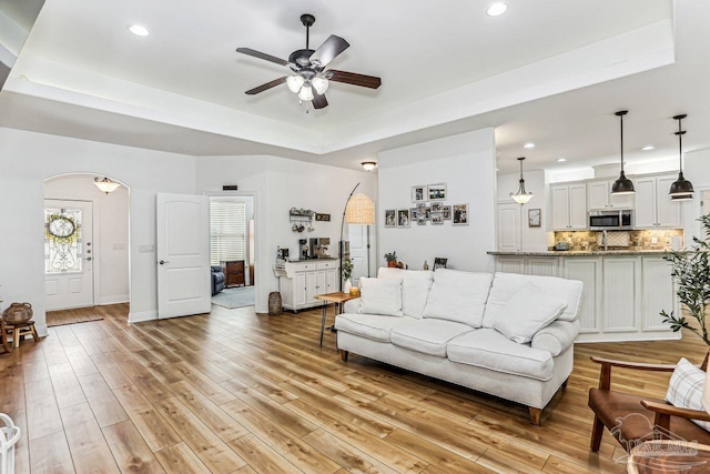 living room with a ceiling fan, arched walkways, recessed lighting, and a raised ceiling