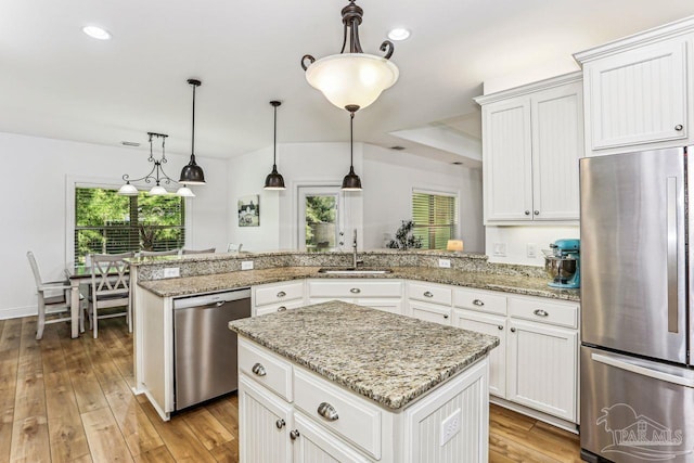 kitchen featuring stainless steel appliances, a peninsula, light wood-style flooring, a sink, and pendant lighting
