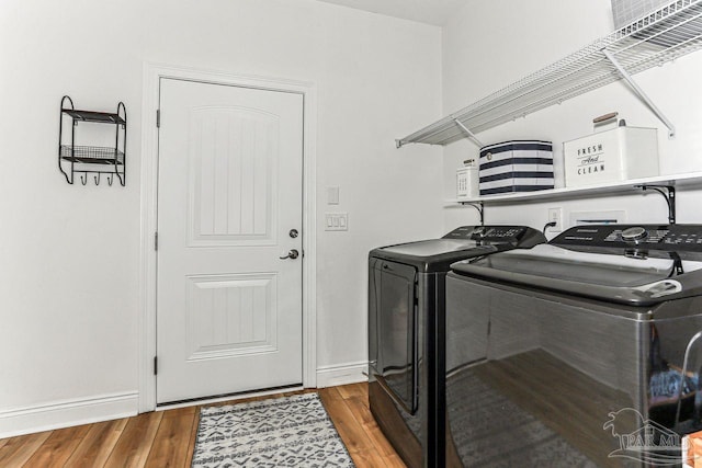 clothes washing area featuring washer and dryer, baseboards, wood finished floors, and laundry area