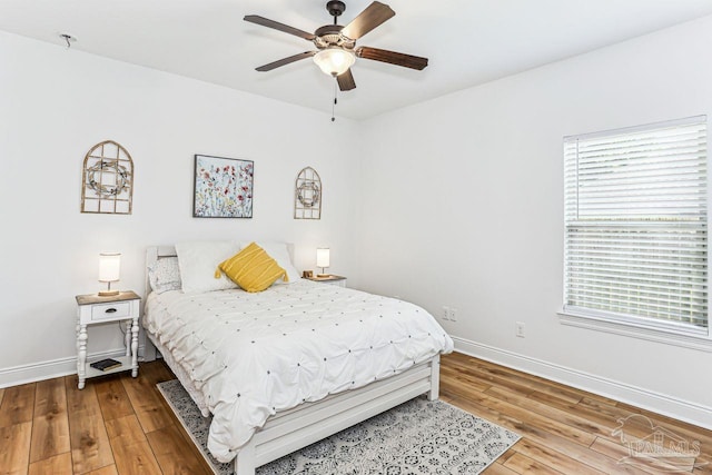 bedroom featuring wood finished floors, baseboards, ceiling fan, and multiple windows