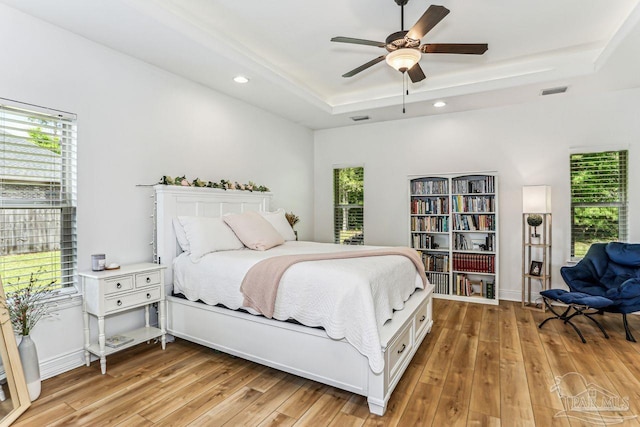 bedroom with light wood finished floors, a tray ceiling, and multiple windows