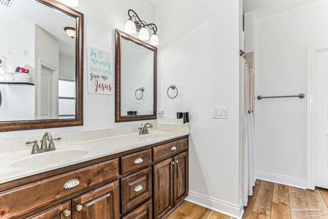 full bath with double vanity, wood finished floors, baseboards, and a sink