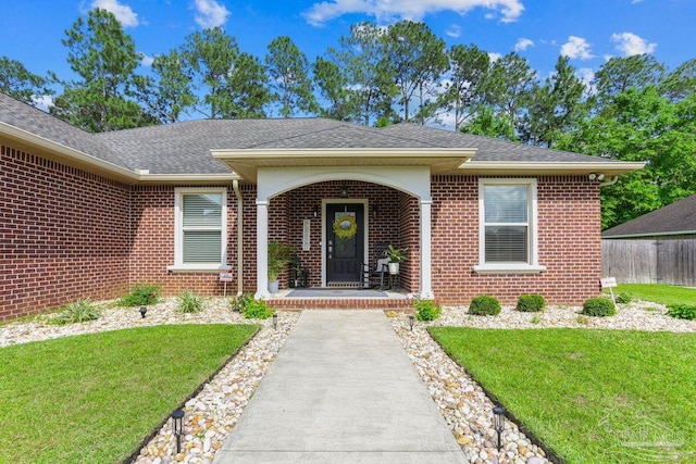 property entrance with brick siding, a porch, a yard, and a shingled roof