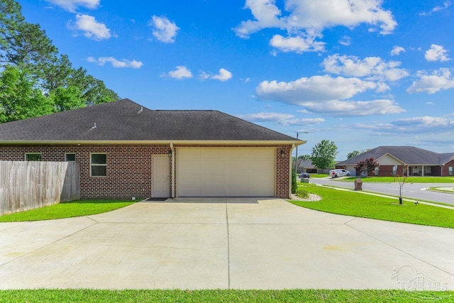 view of side of home with concrete driveway, fence, brick siding, a garage, and a yard