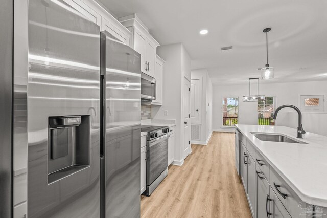 1192 Adrian Way, Milton, FL 32583 - kitchen with stainless steel appliances, a sink, white cabinetry, light wood-style floors, and decorative light fixtures