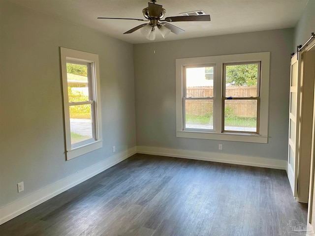 unfurnished room featuring a barn door, ceiling fan, and dark hardwood / wood-style floors