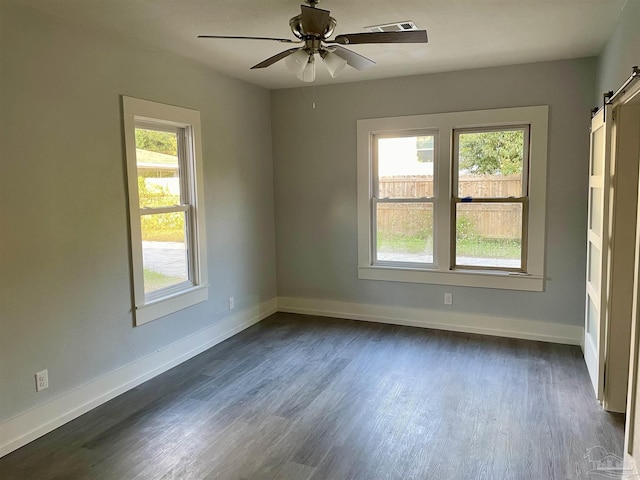 empty room with dark hardwood / wood-style floors, a barn door, and ceiling fan