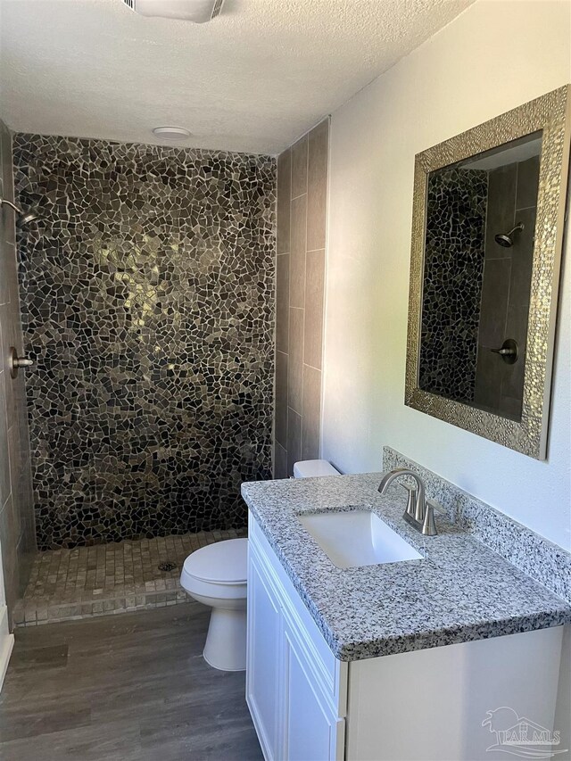 bathroom featuring a textured ceiling, toilet, vanity, hardwood / wood-style flooring, and a tile shower