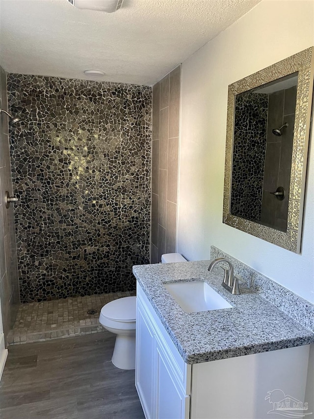 bathroom featuring hardwood / wood-style flooring, vanity, a tile shower, a textured ceiling, and toilet