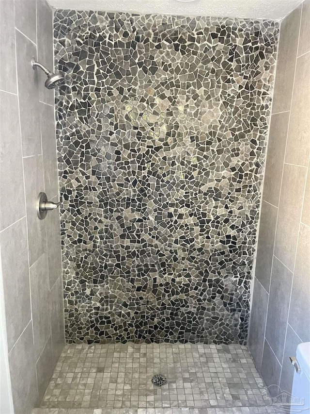 bathroom with a tile shower, toilet, and a textured ceiling