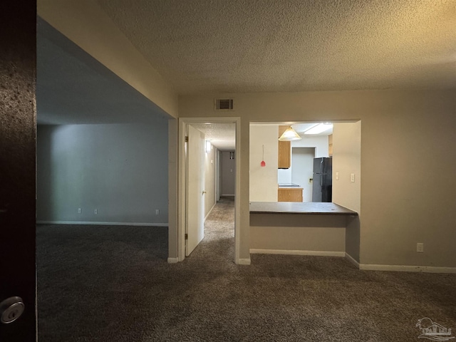 unfurnished room with a textured ceiling, visible vents, baseboards, and dark colored carpet