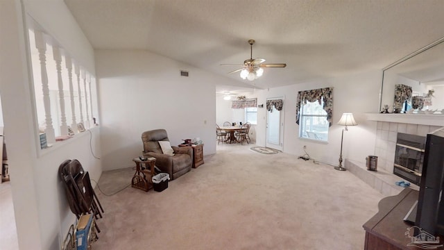 sitting room featuring ceiling fan, a tiled fireplace, light carpet, and vaulted ceiling