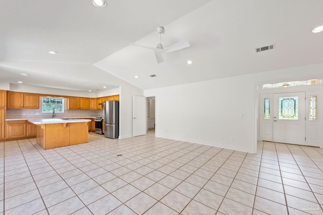 kitchen with lofted ceiling, ceiling fan, light tile patterned floors, appliances with stainless steel finishes, and a kitchen island